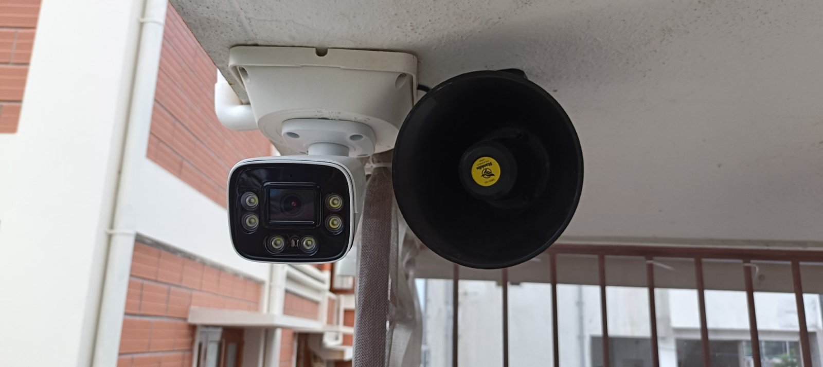 Close-up of a camera with white-light LEDs next to a Stanklin siren speaker under a balcony slab