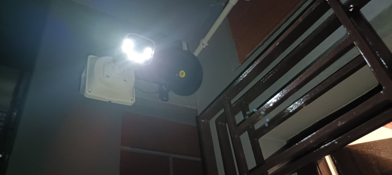 Outdoor camera with bright white-light LEDs lit at night beside a speaker in a stairwell