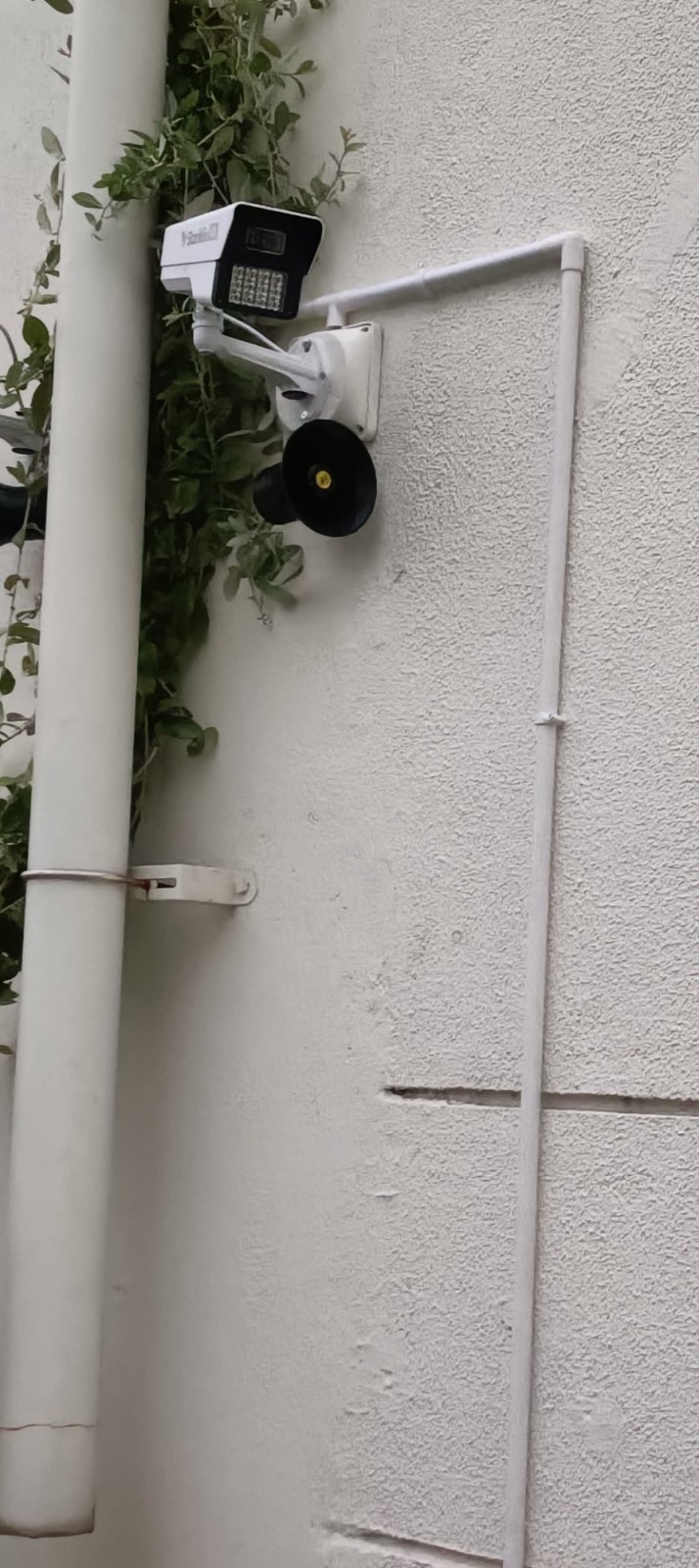 CCTV camera and siren speaker on a wall with cable run down the wall in white conduit
