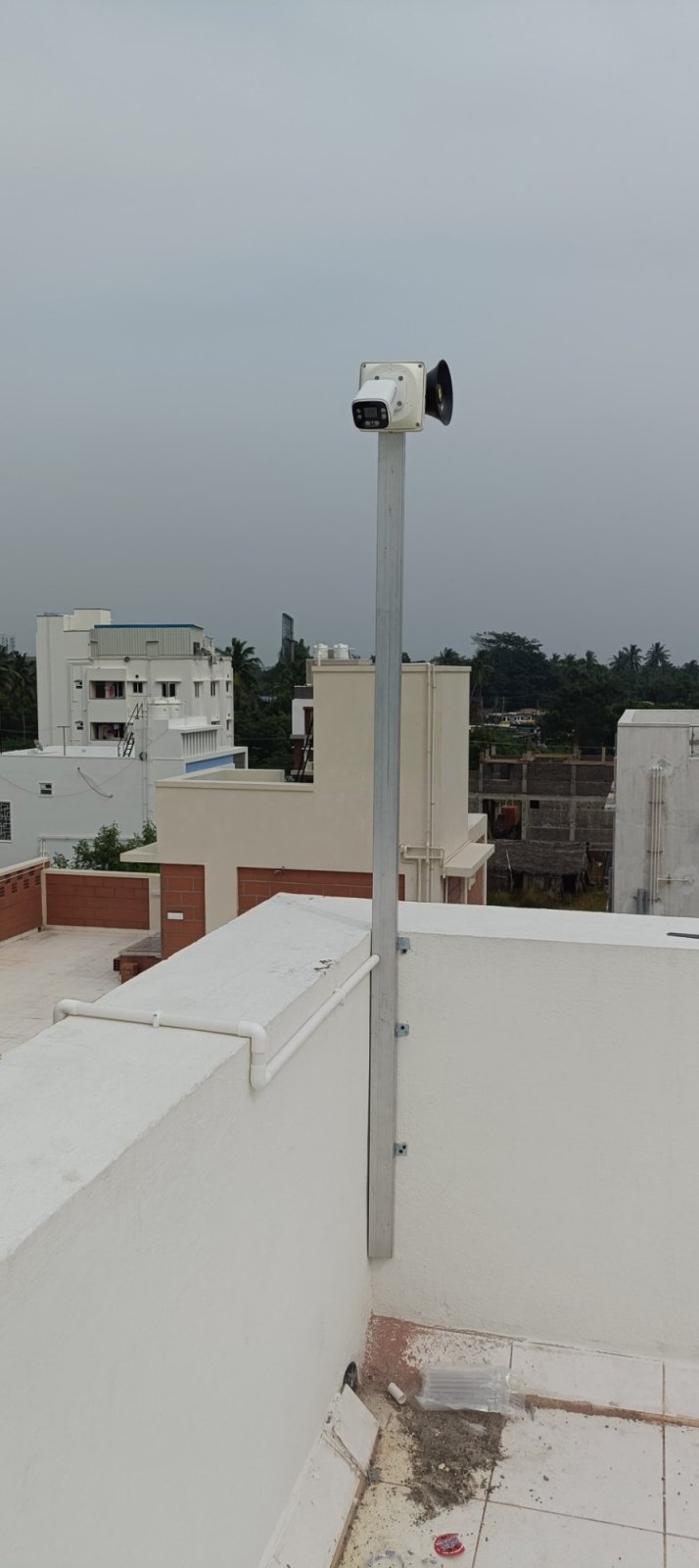 Camera and siren speaker on a pole above a rooftop parapet with cable in conduit