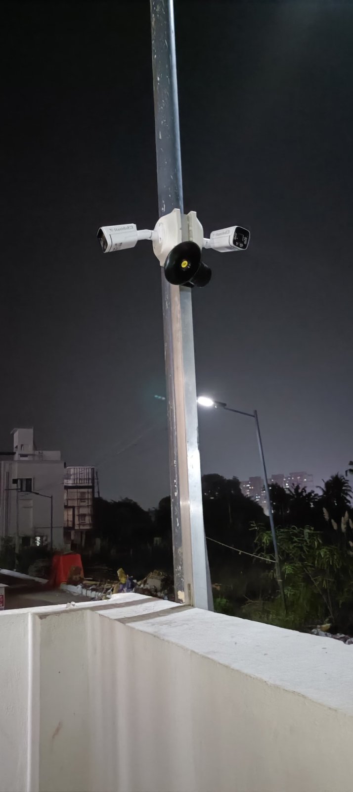 Two Stanklin cameras and a siren speaker on one pole above a terrace wall at night